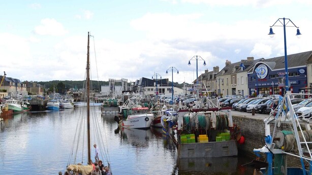 A harbor with boats docked, a pier with a crane, and buildings with shops.