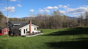 Une maison avec un patio, une grange rouge et une cour couverte d’herbe.