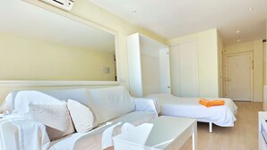 Een moderne, goed verlichte kamer met een witte bank, een klein wit tafeltje en een bed met een oranje handdoek.