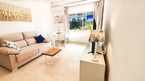A modern living room with a beige sofa, a wooden coffee table, and a dining area with a white table and chairs. - Skol 128 - Great 1-Bedroom Apartment with Sea Views (Marbella)