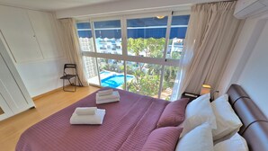 Et hotelværelse med en stor seng, udsigt til en swimmingpool og en balkon.