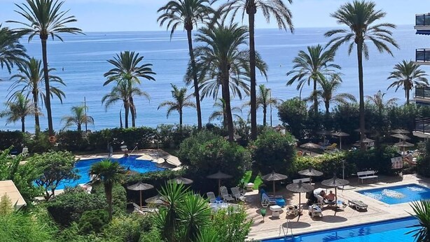 Et resort med flere swimmingpools omgivet af palmer og udsigt over havet.