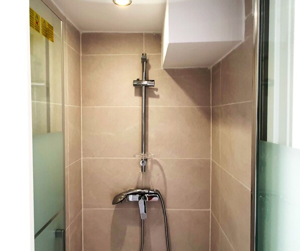 Ducha con cabezal de ducha manual y grifo empotrado en un baño con baldosas color beige.