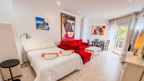 Habitación de hotel con cama, sofás rojos, una mesita, escritorio y obras de arte en las paredes.