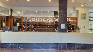 A reception area with a marble counter, a large sign reading "Edificio Sol," and a wooden bookshelf filled with books.