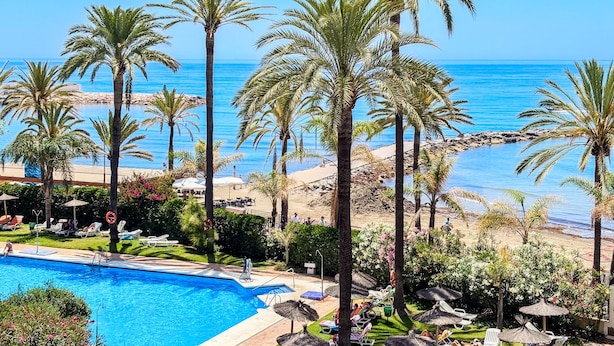 A pool with lounge chairs, palm trees, and a view of the beach and ocean. - Skol 326 - Attractive 1 Bed Apartment with Sea View in Skol Marbella (Marbella)