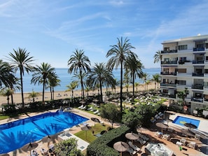 Un complexe hôtelier doté d’une piscine, de chaises longues, de palmiers et offrant une vue sur la plage et l’océan.