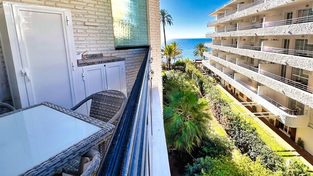 A balcony with wicker furniture, a view of the ocean, and a building with multiple balconies.