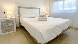 A neatly arranged bedroom with a large bed, two bedside tables with lamps, and a window with sheer curtains.