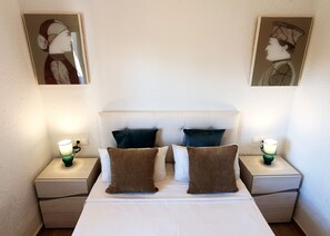 Een hotelkamer met een groot bed, twee nachtkastjes, twee wandlampen en twee ingelijste kunstwerken boven het bed.