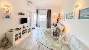 A modern living room with a glass dining table, a sofa, a TV, and artwork on the walls. - Skol 438 - Lovely 1 Bed Apartment with Wi-Fi + Sea Views in Skol Marbella (Marbella)