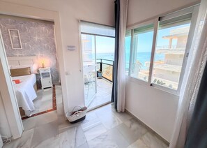 A hotel room with a bed, bedside table, lamp, and a view of the sea through a balcony door.