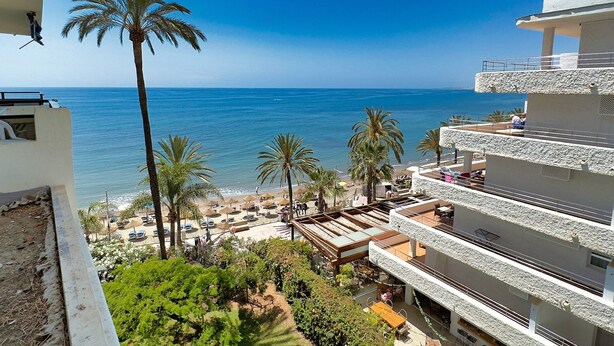 A coastal hotel with a view of the sea, palm trees, and a beach with umbrellas. - Skol 438 - Lovely 1 Bed Apartment with Wi-Fi + Sea Views in Skol Marbella (Marbella)