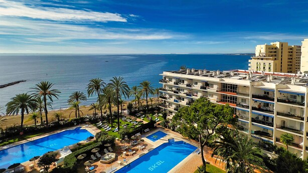 Ein Hotel mit mehreren Schwimmbecken, Meerblick und einem Strandbereich mit Palmen.
