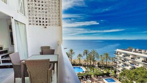 Ein Balkon mit Korbmöbeln, ein Poolbereich mit einem Schild mit der Aufschrift 'SKOL' und Blick aufs Meer.