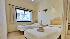 Una habitación de hotel con dos camas, una ventana con cortinas, una mesita de noche y una lámpara fijada en la pared.