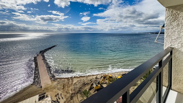 Un balcone con vista sul mare, su una costa rocciosa e un cielo sereno.