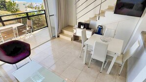 Ein modernes Wohnzimmer mit Glastisch, weißen Stühlen, einer Couch und einer Treppe, die zu einem Balkon mit Stadtblick führt.