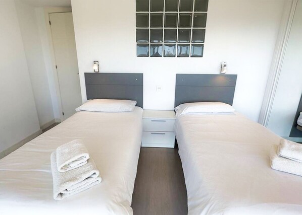 A hotel room with two single beds, a small window, and a nightstand with a lamp.