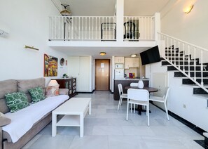 A modern apartment with a living room, dining area, kitchen, and a staircase.
