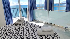 Una camera d'albergo con un letto, un balcone con una porta vetrata e vista mare.