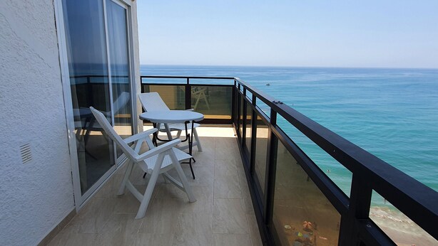 Un balcone con vista sull'oceano, sedie in plastica bianca, un tavolino rotondo e una porta in vetro.