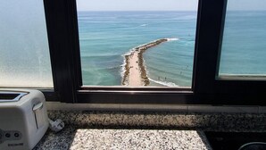 Vista sull'oceano attraverso una finestra, con un molo frangiflutti roccioso in evidenza.