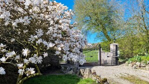 Un jardin avec un mur de pierre, un portail en métal et un chemin menant à un bâtiment.