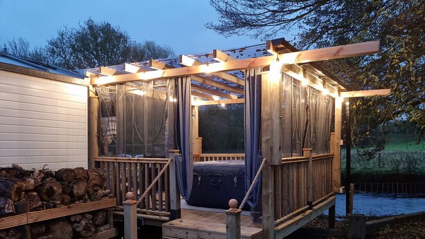 Une terrasse en bois dotée d’un espace salon couvert, d’un escalier et d’une vue sur un plan d’eau.