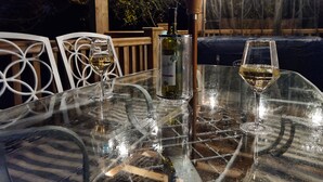 Un espace de restauration en plein air avec une table en verre, deux verres à vin et une bouteille de vin.
