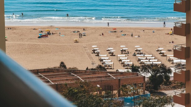 A beach with umbrellas and lounge chairs, a wooden structure, and a view of the ocean.