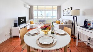 A dining area with a round table set for four, a television, and a sofa in the background.