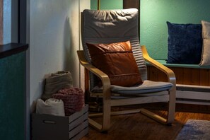 Ein Zimmer mit einem Holzstuhl, einem Kissen, einem kleinen Teppich und einer Aufbewahrungsbox.
