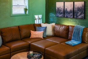 A brown leather sectional sofa with multiple cushions, a small round table with a candle, and a wall with three framed pictures. - Dreamy Forest Vibe Loft for Couples, Deck and Parking (Pittsburgh)