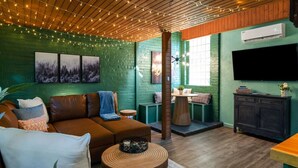 A cozy living room with a brown leather sofa, a round wooden coffee table, and a green brick wall. - Dreamy Forest Vibe Loft for Couples, Deck and Parking (Pittsburgh)