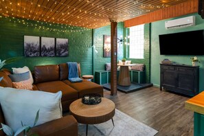Ein gemütliches Wohnzimmer mit einem braunen Ledersofa, einem runden Holztisch und einer Wand aus grünen Ziegeln.