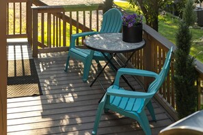 Eine Holzterrasse mit einem runden Tisch, zwei Stühlen, einem Blumentopf und einem kleinen Baum.