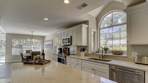 A modern kitchen with a large island, stainless steel appliances, and a view of the outdoors through large windows. - New Listing Wonderful Updated Home. Bikes & Beach Gear included (Hilton Head Island)