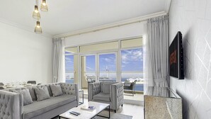 Ein modernes Wohnzimmer mit einer Couch, Sesseln, einem Couchtisch und einem an der Wand befestigten Fernseher.
