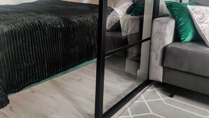 A modern bedroom with a bed, a grey sofa, a glass partition, and a hanging light fixture. - Apartament Glamour - 365PAM (Kolobrzeg)