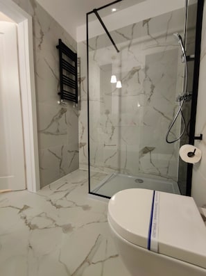 Een moderne badkamer met een douchecabine van glas, marmeren vloeren en een toilet met een blauwe streep.