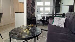 A modern living room with a dark-colored sofa, a round black table with a gold decorative item, and a patterned rug. - Apartament Glamour - 365PAM (Kolobrzeg)