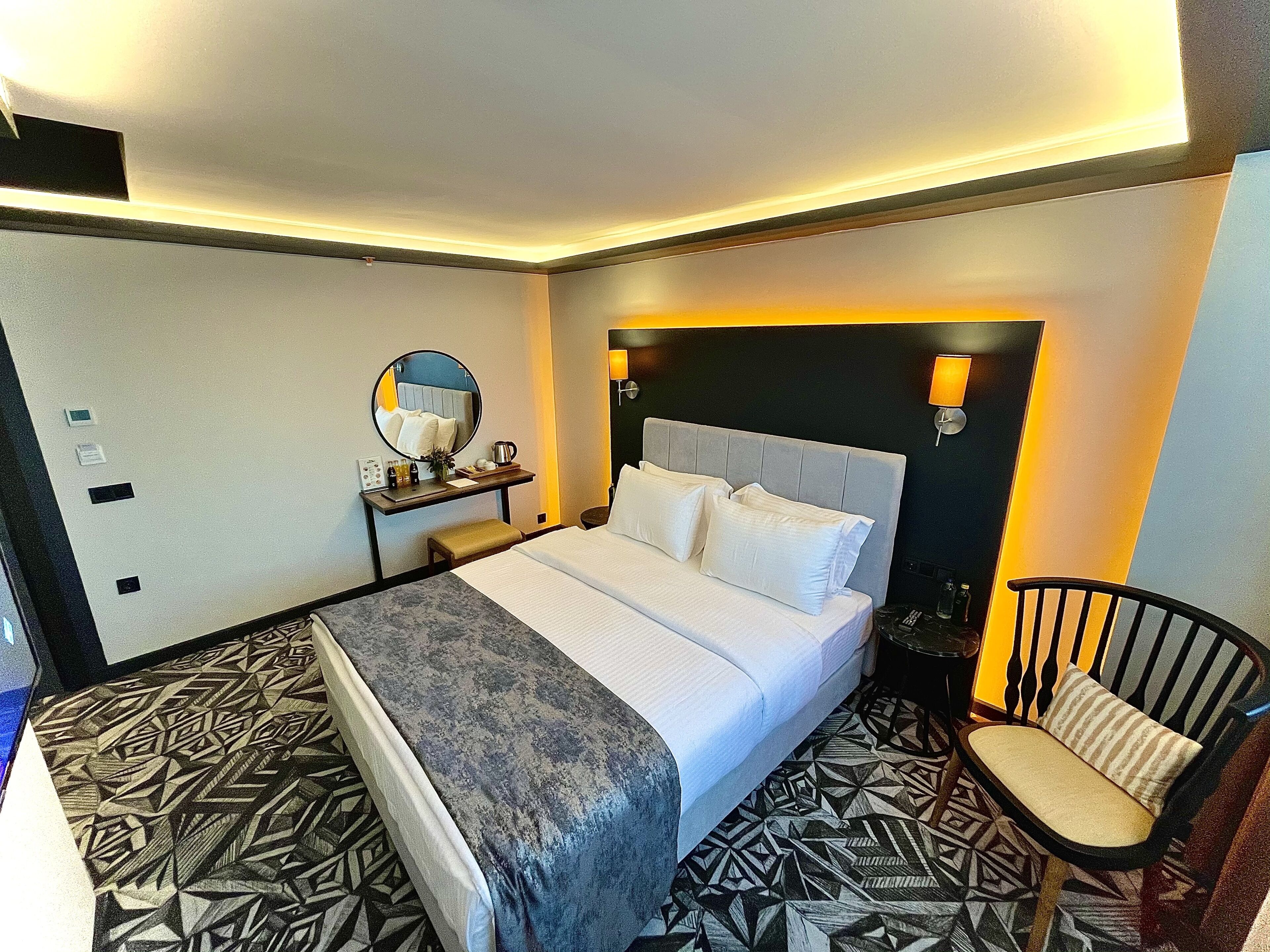 A hotel room with a bed, bedside table, chair, and geometric patterned floor.