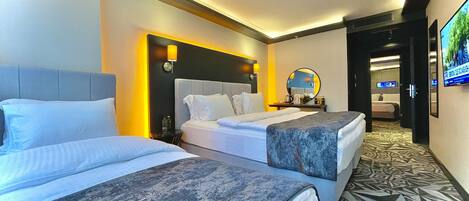 A hotel room with two beds, a bedside table with a lamp, a mirror, and a television on the wall.
