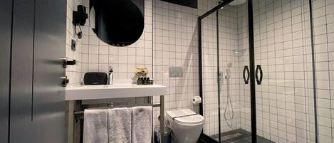 A modern bathroom with a white tiled wall, a black bathtub, a glass shower enclosure, and a white toilet.