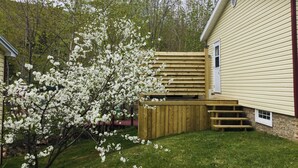 Um imóvel residencial com deck de madeira, um pequeno jardim e uma casa com revestimento bege e detalhes em vermelho.