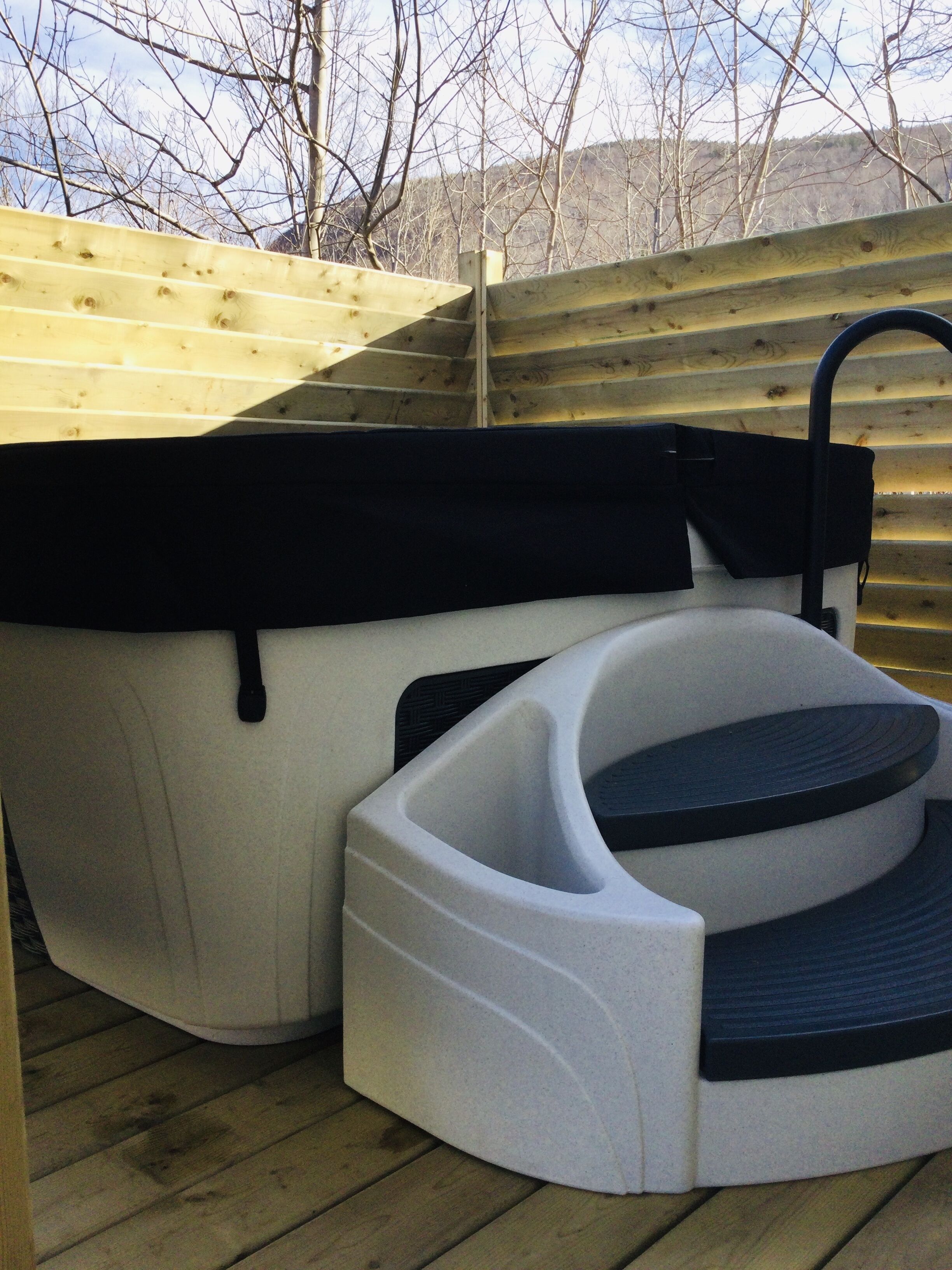 A hot tub with a black seat and a black cover, placed on a wooden deck.