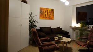 Un salon avec un canapé, deux fauteuils, une table basse et un tableau accroché au mur.