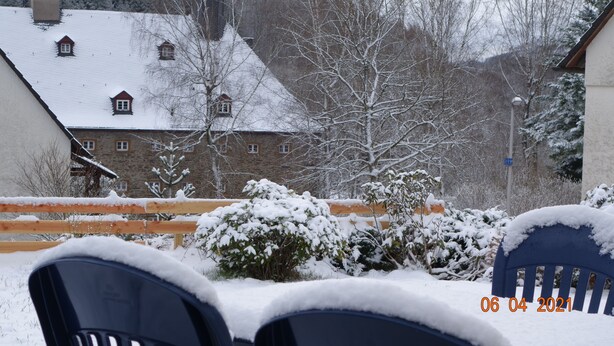 Un espace extérieur aménagé avec des sièges, recouvert de neige, et offrant une vue sur un bâtiment doté de nombreuses fenêtres et d’une cheminée.