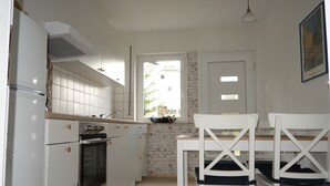 Une cuisine compacte avec des meubles blancs, un four encastré et une fenêtre donnant sur un bâtiment à l’extérieur.